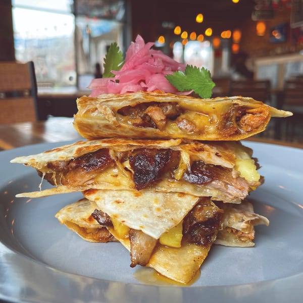 Stack of Taqueria Picoso quesadillas with melted cheese, meat, and pickled onions on a blue plate.