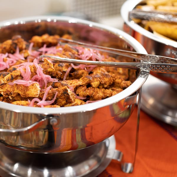 Chafing dish filled with seasoned chicken and pickled red onions, with serving tongs.