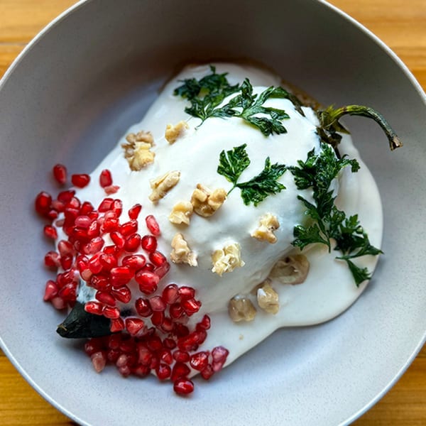 Chiles en nogada, a Mexican dish, topped with white sauce, pomegranate seeds, and parsley.