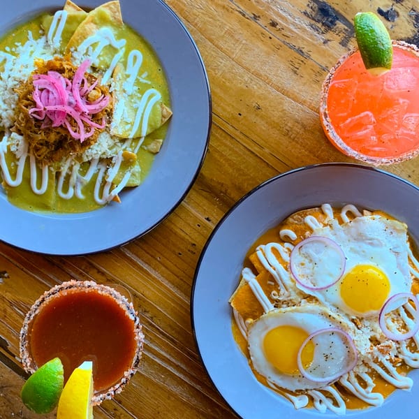 Two plates of Mexican chilaquiles with drinks on a wooden table at Taqueria Picoso.